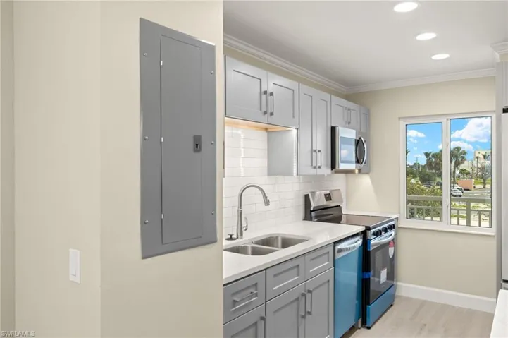 Kitchen with appliances with stainless steel finishes, a sink, baseboards, backsplash, and light wood finished floors