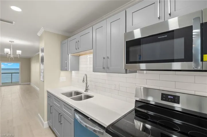 Kitchen featuring stainless steel appliances, a sink, crown molding, baseboards, and a chandelier