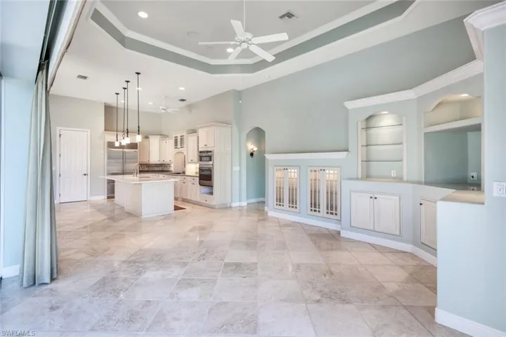 Kitchen with a center island with sink, hanging light fixtures, a tray ceiling, ceiling fan, and a kitchen bar