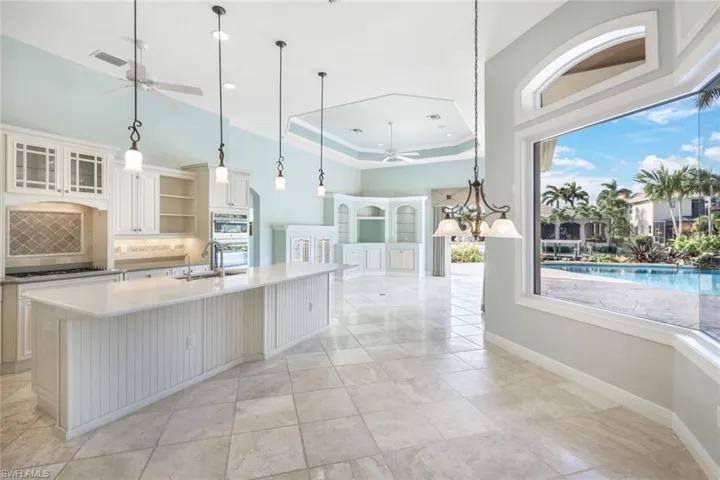 Kitchen featuring a tray ceiling, ceiling fan with notable chandelier, pendant lighting, and light tile patterned floors