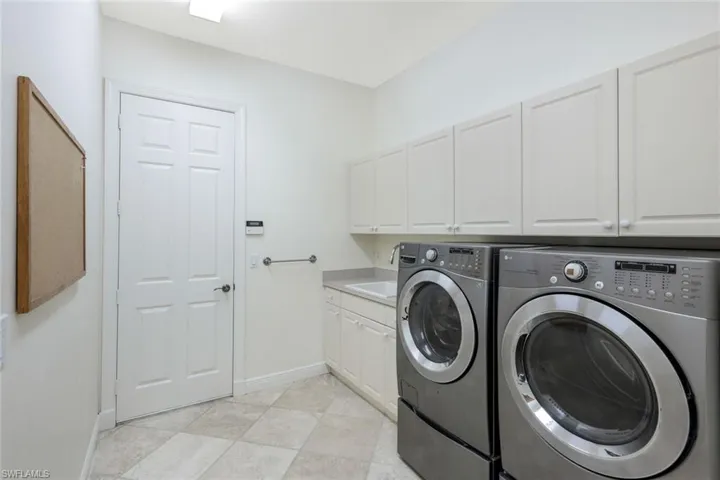 Laundry room featuring washing machine and clothes dryer, cabinets, light tile patterned floors, and sink