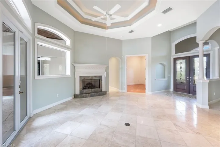 Unfurnished living room with light tile patterned floors, ceiling fan, french doors, ornate columns, and a fireplace