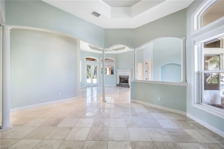 Spare room with light tile patterned floors, a tray ceiling, ornate columns, and a high ceiling