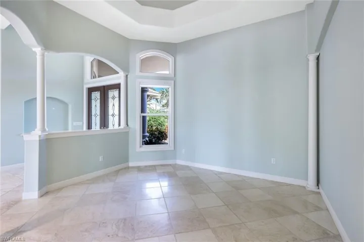 Empty room with decorative columns, french doors, crown molding, light tile patterned flooring, and a tray ceiling