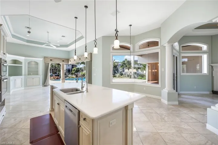 Kitchen with a center island with sink, stainless steel appliances, a tray ceiling, sink, and decorative light fixtures