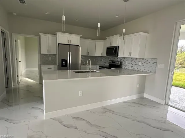 Kitchen featuring stainless steel appliances, a peninsula, white cabinetry, tasteful backsplash, and light marble finish flooring