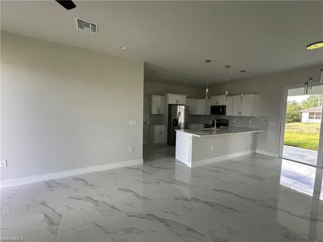 Kitchen with light marble finish floors, open floor plan, backsplash, white cabinetry, and a peninsula