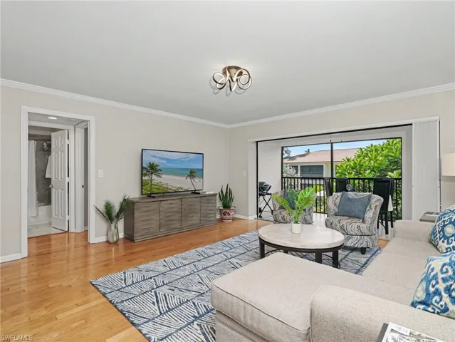 Bright living area featuring wood-finish flooring, crown molding, and a sliding glass door opening to a screened balcony