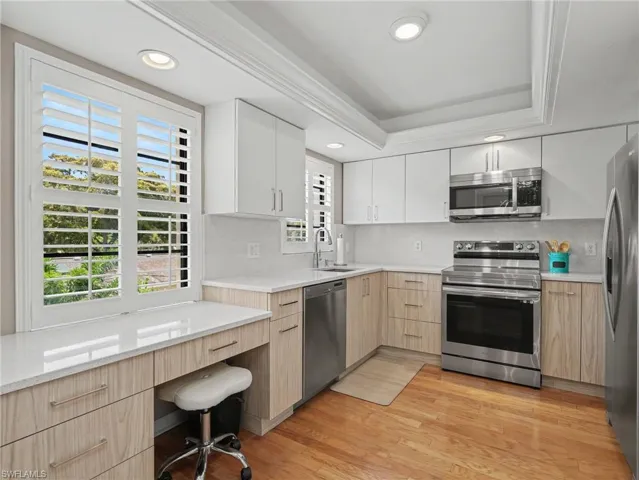 Modern kitchen featuring two-tone cabinetry with white upper cabinets and wood-finish lower cabinets, light-toned countertops, hardwood flooring, recessed lighting, and stainless steel appliances