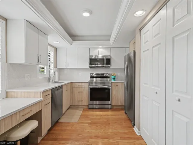 Modern kitchen featuring stainless steel appliances, light wood-finish lower cabinetry, white upper cabinetry, white countertops, and wood-finish flooring