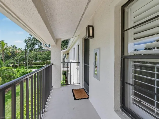 Private balcony with dark metal railings, textured white exterior, modern wall sconce, and white louvered window treatments