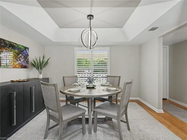 Dining space featuring a modern chandelier, tray ceiling, and plantation shutters