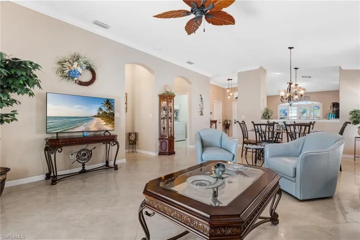 Living room featuring arched walkways, ornamental molding, ceiling fan, hanging lights, and view into laundry room with washer / clothes dryer