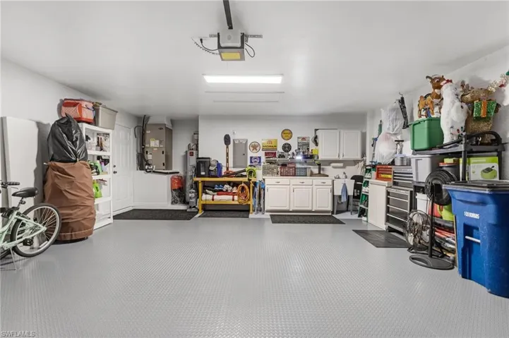 Garage with heating unit, electric panel, a workshop area, water heater, and a garage door opener