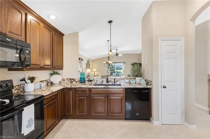 Kitchen featuring black appliances, lofted ceiling, light stone counters, light tile patterned floors, and suspended lighting