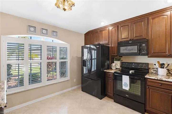 Kitchen with black appliances, light stone countertops, healthy amount of natural light, and light tile patterned floors