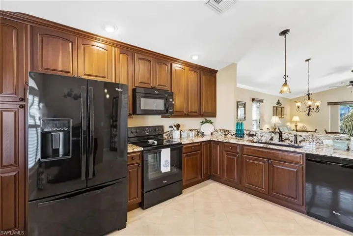 Kitchen with black appliances, light stone countertops, ornamental molding, a chandelier, and plenty of natural light
