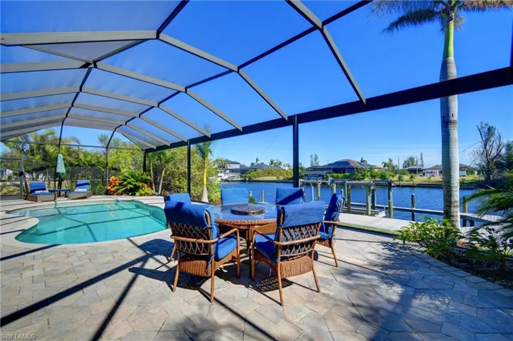 View of pool with glass enclosure, a dock, a water view, and a patio