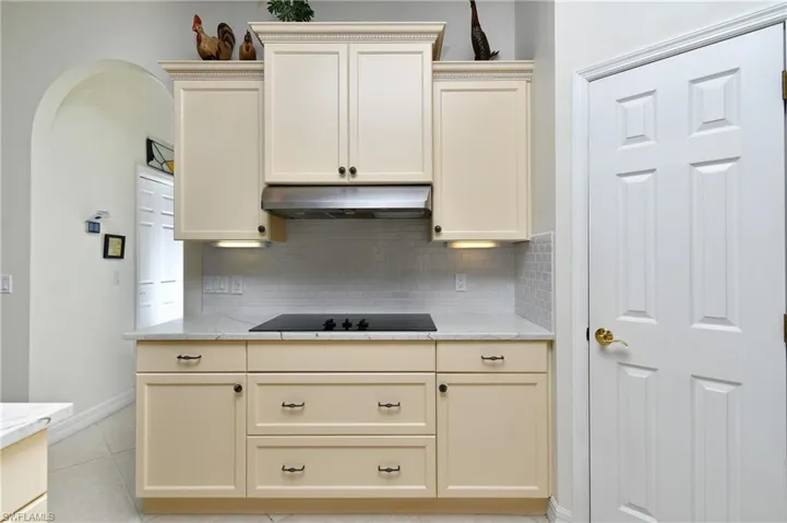 Kitchen featuring decorative backsplash, cream cabinets, black electric cooktop, and light tile patterned flooring
