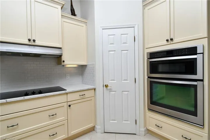 Kitchen with cream cabinets, black electric cooktop, tasteful backsplash, light tile patterned flooring, and stainless steel double oven