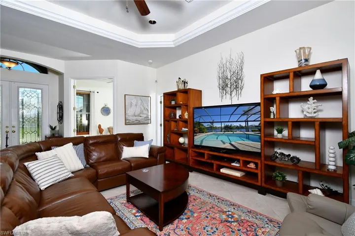 Tiled living room with french doors, a raised ceiling, ceiling fan, and ornamental molding