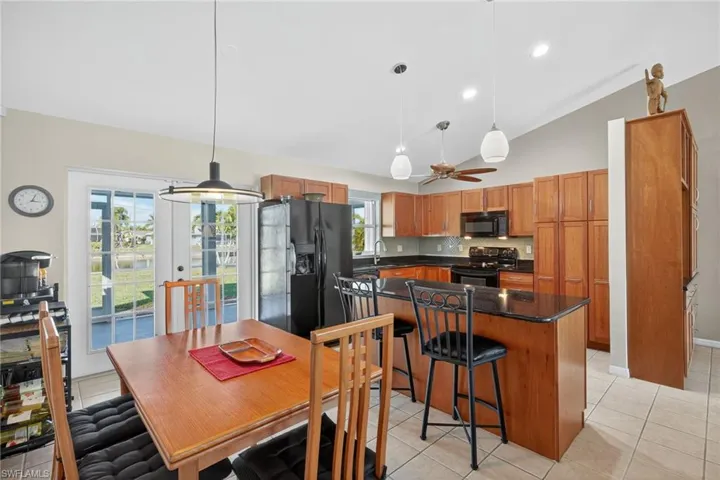 Kitchen featuring light tile patterned flooring, pendant lighting, black appliances, a kitchen island, and high vaulted ceiling