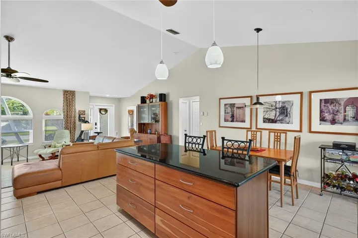Kitchen with a ceiling fan, hanging light fixtures, brown cabinetry, a center island, and light tile patterned floors