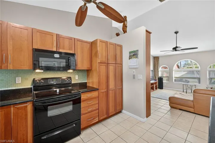 Kitchen featuring black appliances, a ceiling fan, backsplash, dark stone counters, and light tile patterned flooring