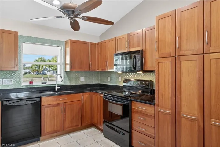 Kitchen featuring black appliances, vaulted ceiling, backsplash, light tile patterned floors, and dark stone counters
