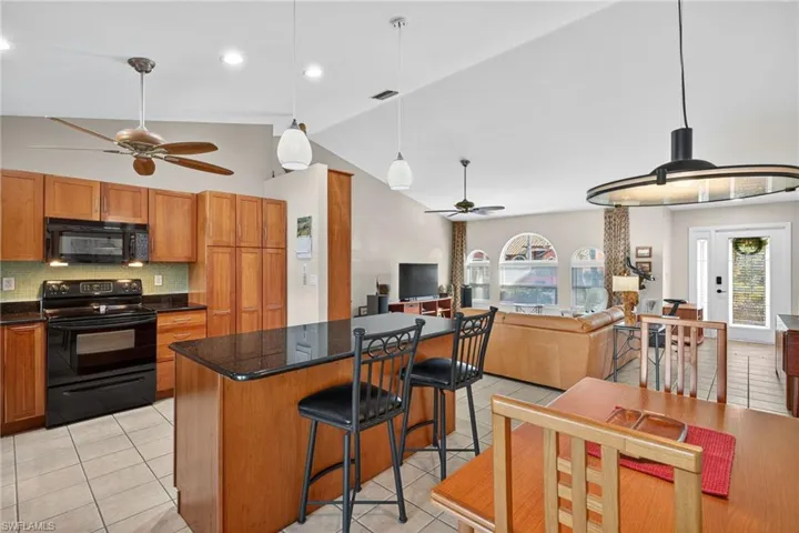 Kitchen featuring pendant lighting, black appliances, open floor plan, ceiling fan, and high vaulted ceiling