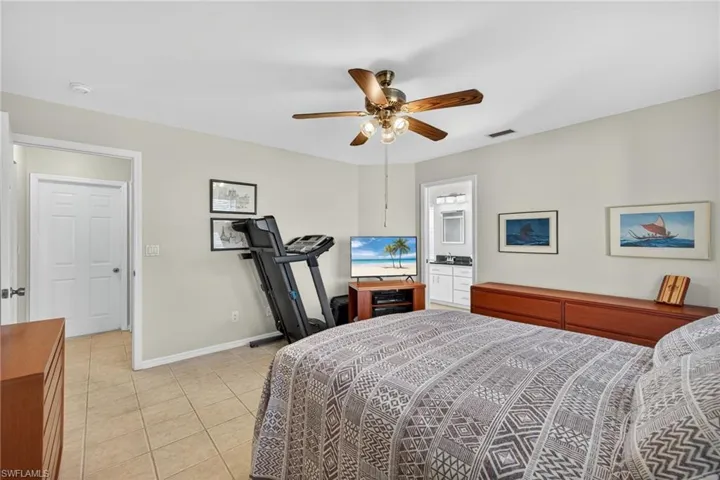 Bedroom featuring light tile patterned floors, ceiling fan, and ensuite bath