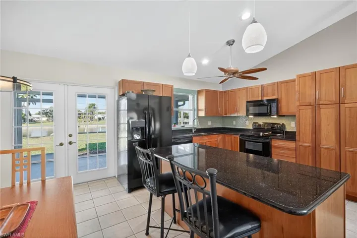 Kitchen featuring a kitchen bar, decorative light fixtures, black appliances, dark stone countertops, and french doors