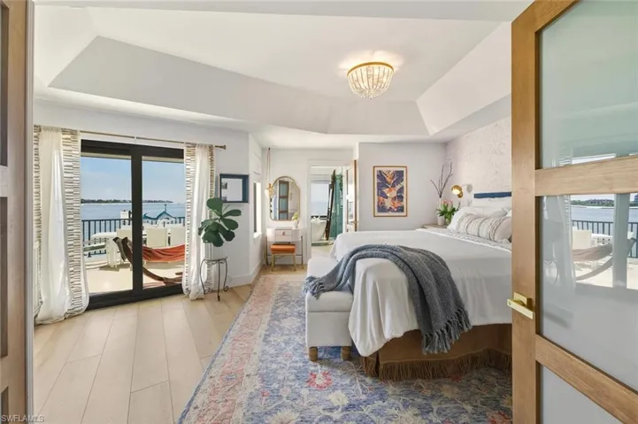 Bedroom with access to outside, a water view, light wood-style floors, a tray ceiling, and a chandelier