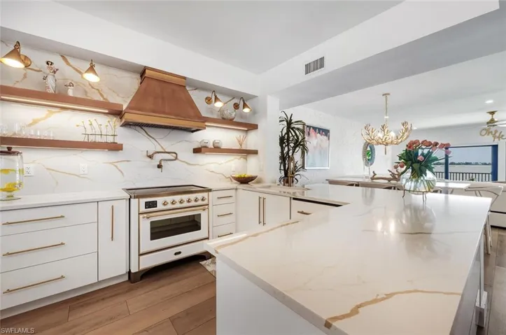 Kitchen featuring open shelves, light stone counters, white cabinets, tasteful backsplash, and custom range hood