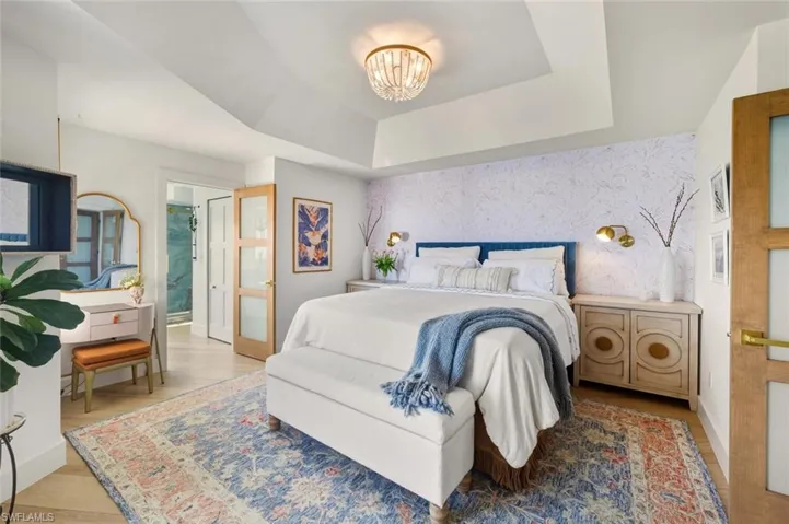 Bedroom featuring wallpapered walls, ensuite bathroom, light wood finished floors, a chandelier, and a tray ceiling