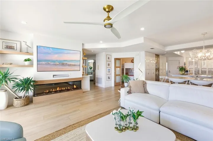 Living area with a ceiling fan, a chandelier, wood finished floors, a glass covered fireplace, and recessed lighting