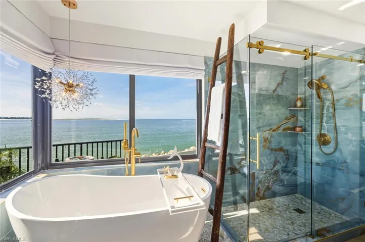 Bathroom featuring a freestanding tub, a marble finish shower, a water view, and a chandelier