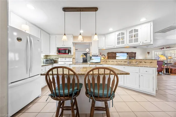 Kitchen with a kitchen bar, white cabinetry, light stone countertops, and glass insert cabinets