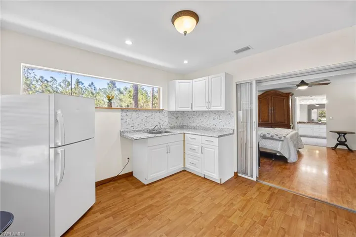 Kitchen featuring freestanding refrigerator, white cabinets, light wood-style floors, recessed lighting, and backsplash