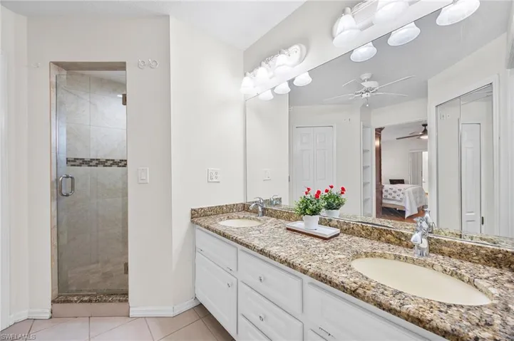 Bathroom with ensuite bathroom, double vanity, a shower stall, ceiling fan, and light tile patterned floors