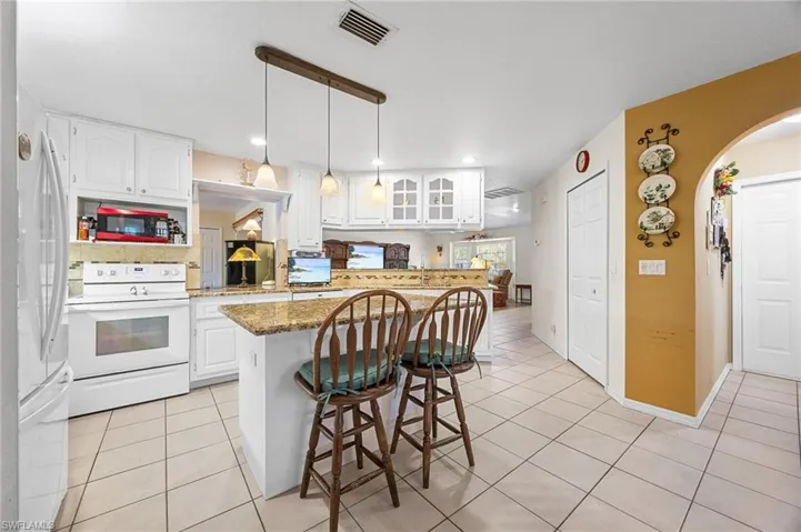 Kitchen with white cabinetry, a kitchen breakfast bar, white appliances, light tile patterned floors, and dark stone counters
