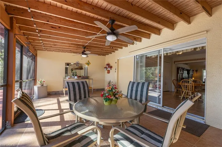Sunroom featuring outdoor dining area, ceiling fan, beamed ceiling, and a patio