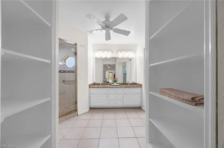 Bathroom with a stall shower, double vanity, light tile patterned floors, ceiling fan, and a closet