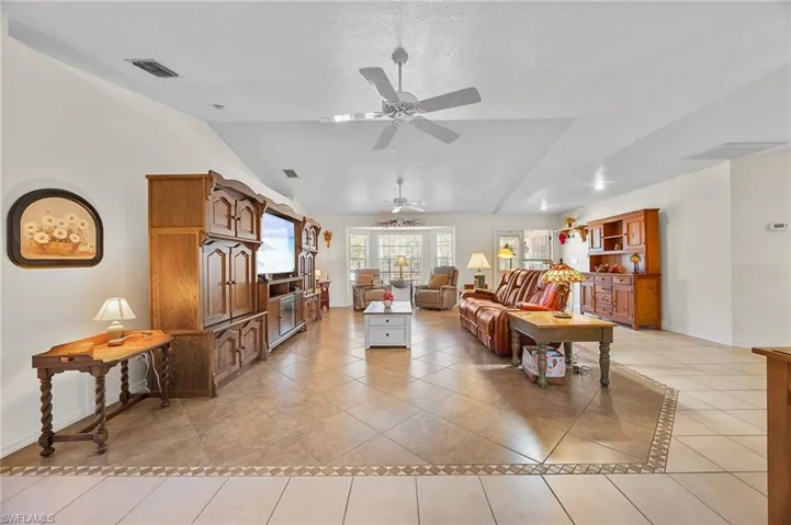 Living area featuring ceiling fan, light tile patterned floors, and lofted ceiling