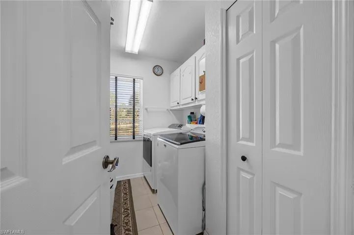 Laundry room featuring light tile patterned flooring, cabinet space, washer and clothes dryer, and a textured ceiling