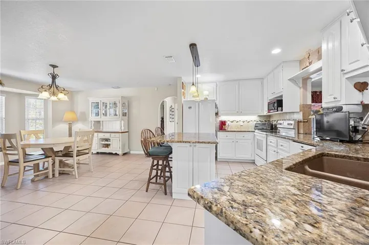 Kitchen featuring white cabinetry, dark stone counters, a breakfast bar, backsplash, and white appliances