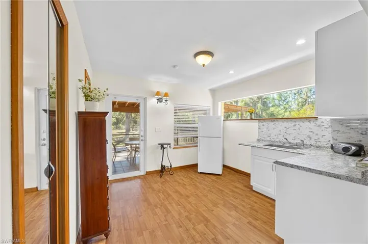 Kitchen featuring freestanding refrigerator, light countertops, light wood-style flooring, decorative backsplash, and white cabinetry