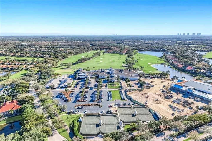 Aerial perspective featuring a multi-court tennis complex, golf course fairways, expansive water elements, and a centralized clubhouse facility