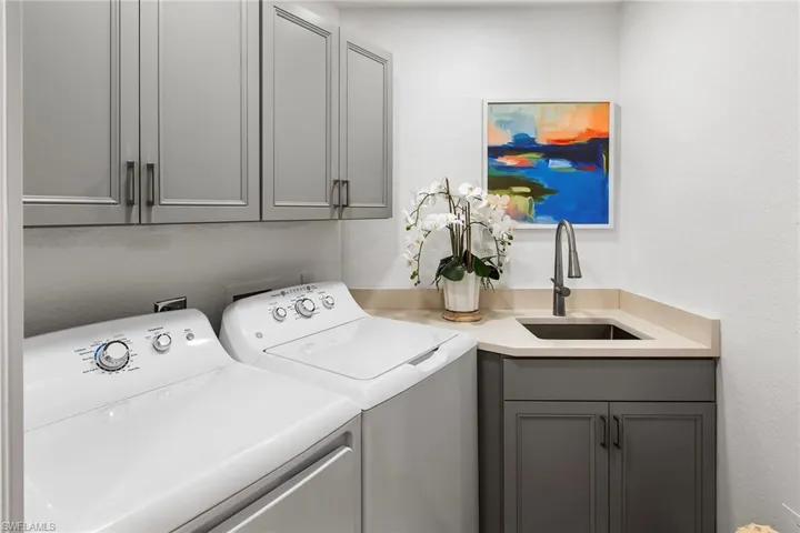 Washroom featuring washing machine and clothes dryer, cabinet space, and a sink