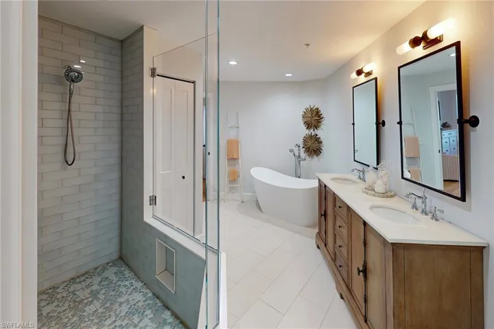Bathroom featuring a tile shower, double vanity, a sink, and a freestanding tub